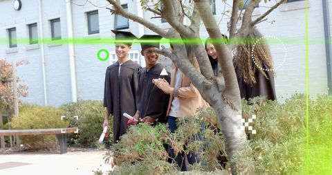 Graduates smiling and celebrating with mentor in courtyard wearing gowns and mortarboards