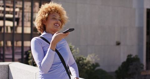African American woman leaning on urban terrace speaking into smartphone, smiling