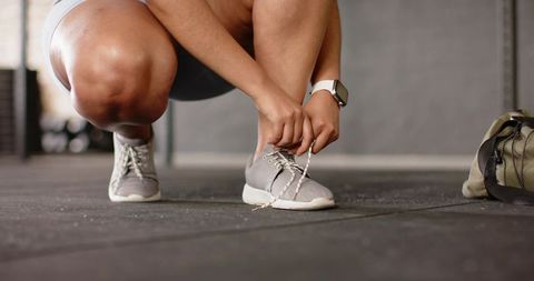 Athlete tying shoelaces before workout wearing smartwatch and gym shorts