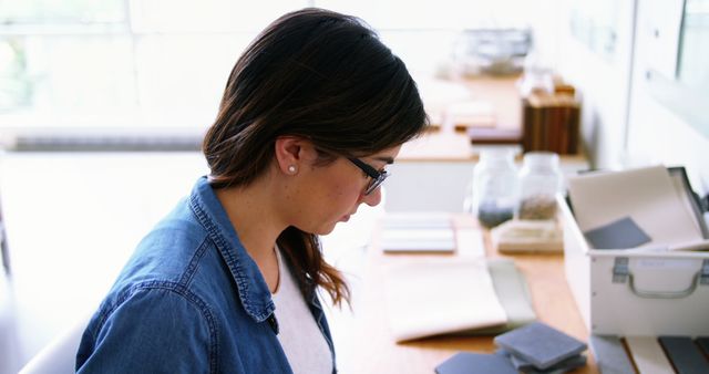 Woman is working at desk in bright home office, suggesting a remote work or freelance setting. Ideal for illustrating topics on productivity, remote work, home offices, creative professions, and focused work environments.