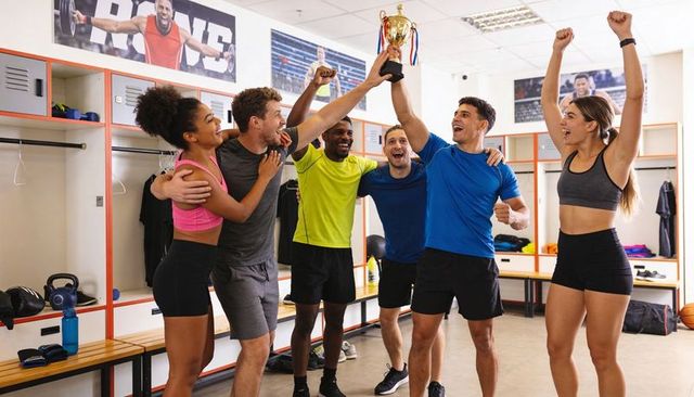 Diverse team celebrating victory hoisting gold trophy in locker room after game