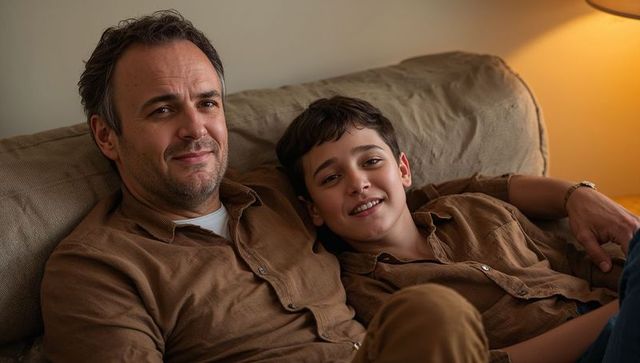 Father and Teen Son Relaxing on Sofa Wearing Matching Brown Shirts Sharing Warm Evening