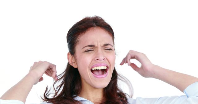 A young Caucasian woman appears frustrated or annoyed, plugging her ears and screaming, with copy space. Her expression and gesture suggest she is trying to block out a loud noise or expressing exasperation.