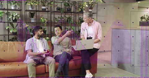 Woman opening laptop leading casual team discussion in modern plant-filled lounge workspace