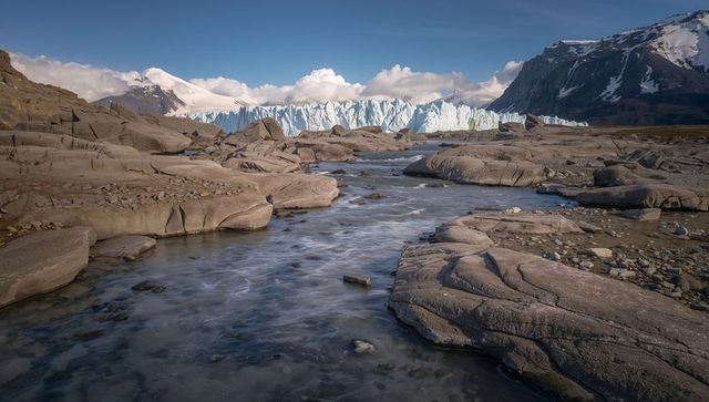 Flowing meltwater stream leading to jagged glacier terminus in rugged alpine valley