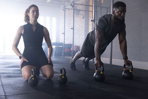 Diverse partners performing kettlebell plank in backlit gym for strength training