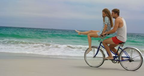 Joyful Couple Riding Bicycle Along Sandy Beach Shore
