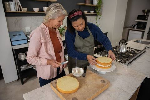 Two women assembling layered cake together in modern kitchen — baking friendship moment