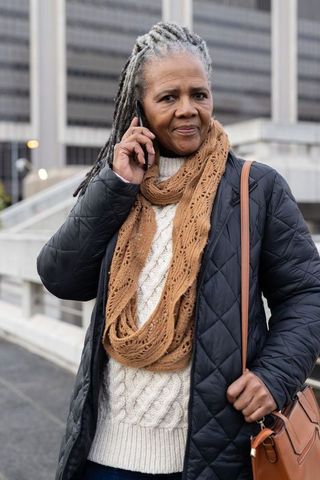 Senior african american woman talking on phone wearing knit scarf and puffer coat in urban plaza