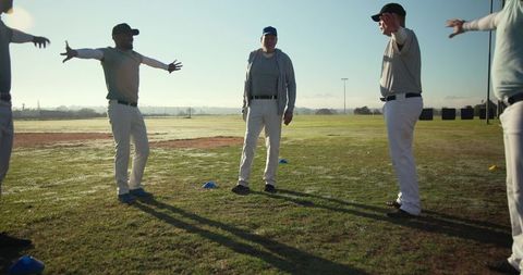 Senior coach leading baseball team stretching drill on dewy morning practice field