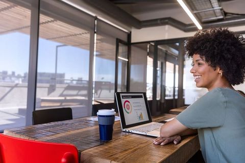 Smiling african american woman working on laptop with charts in modern coworking space