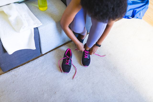 African american mid adult woman tying shoelace of sports shoe at home. unaltered, lifestyle, fitness, healthy lifestyle, preparation, wellbeing.