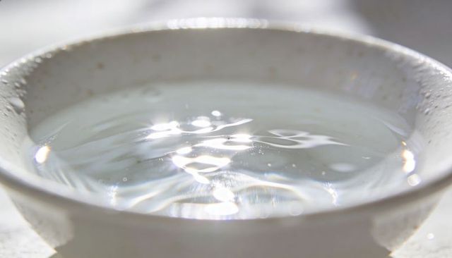 Sunlit ceramic bowl holding rippling clear water with sparkling reflections and bokeh