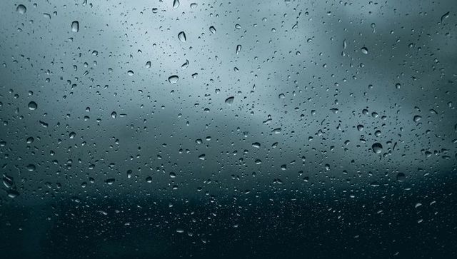 Raindrops clinging to car window glass, blurred horizon and moody overcast sky