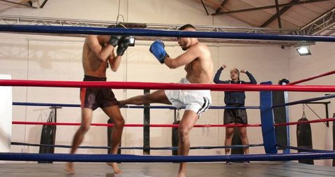 Boxer delivering powerful roundhouse kick while opponent guarding and coach instructing