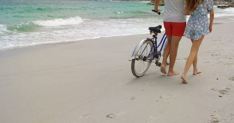 Couple Walking with Bicycle Along Ocean Shore