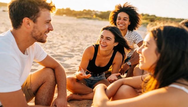 Young friends laughing and chatting on beach at golden hour, casual group relaxing together