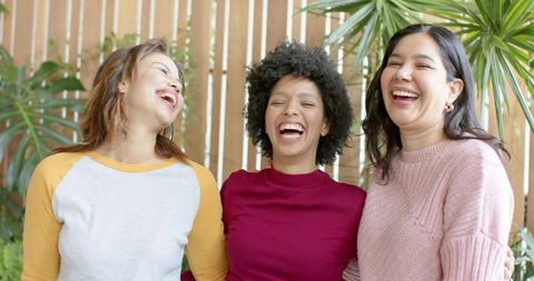 Diverse women laughing and embracing in casual knit sweaters with indoor plants