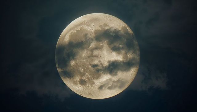 Luminous full moon with cloud shadows in night sky