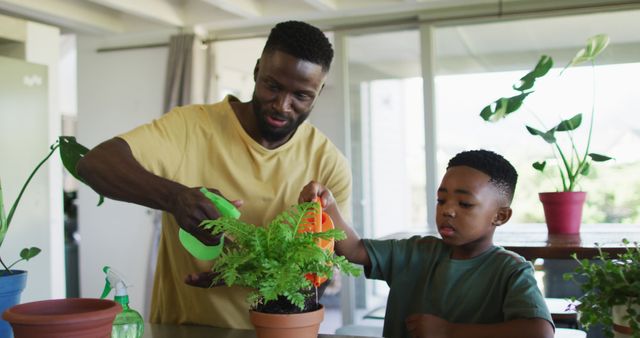 African american father and son watering plant pot together at home. family father son togetherness relationship concept