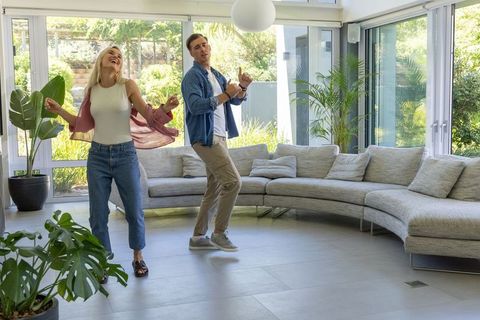 Couple dancing joyfully in sunlit modern living room with curved sectional sofa and greenery