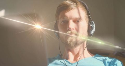 Man in headphones working intensely on laptop in sunlit room