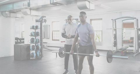 Male Trainee Lifting Barbell Deadlift with Trainer Coaching in Bright Industrial Gym Studio