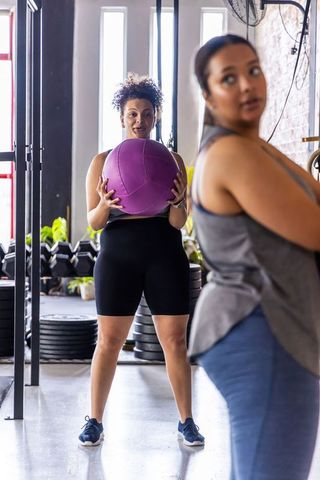 Diverse women training in gym, focused woman holding purple medicine ball during workout