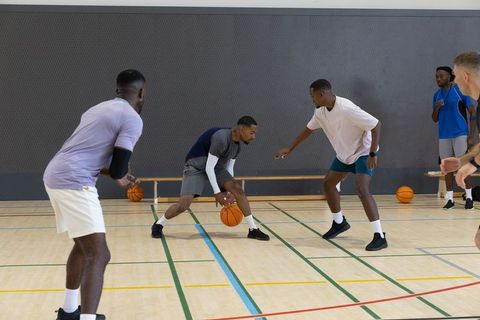 Men practicing basketball dribbling and defense on indoor hardwood court during team training sessio
