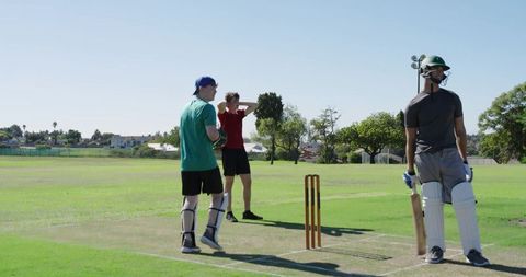 Cricket batter holding bat at crease during practice on sunny green outfield