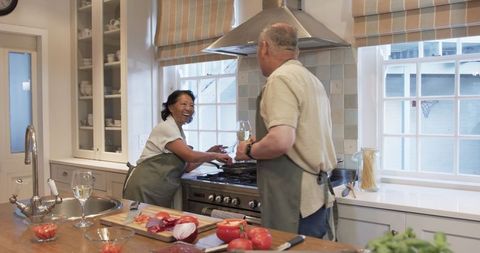 Senior Couple Joyfully Cooking and Sharing Wine in Kitchen