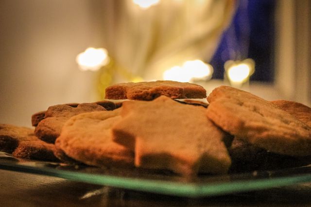 Homemade star-shaped cookies placed on a glass plate in warm ambient light with bokeh lights in the background. Suitable for use in holiday baking advertisements, cooking blogs, Christmas and holiday-themed promotions, and articles focusing on festive treats or homemade desserts.