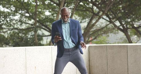 Senior African American professional celebrating while checking smartphone on urban plaza