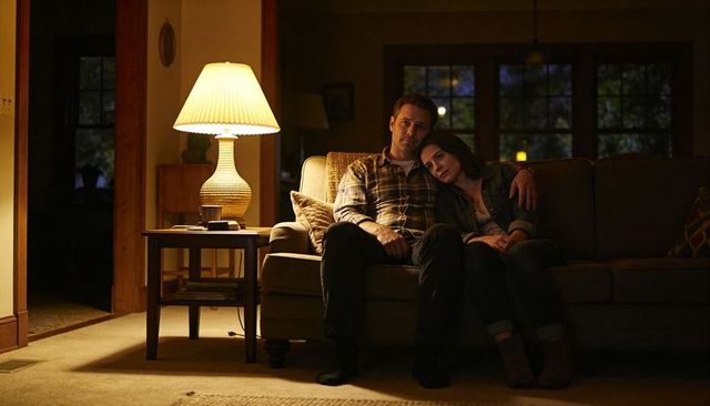 Couple cuddling on sofa at night with warm lamp glow creating cozy intimate living room scene