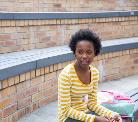 African american student sitting on tiered brick bench with backpack looking thoughtful