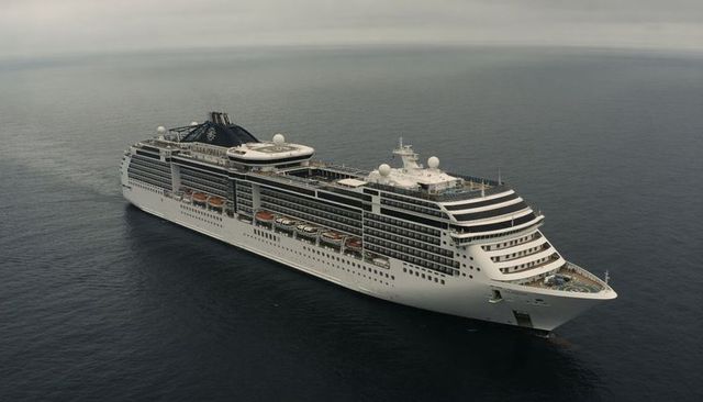 Luxury cruise ship gliding across calm open ocean with lifeboats, helipad and overcast sky