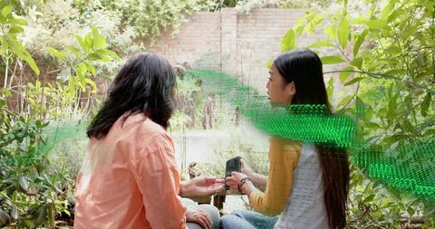 Two women checking backyard faucet while sharing smartphone and discussing garden tasks