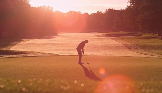 Backlit golfer putting during golden hour sunrise with lens flare dewy bokeh silhouette