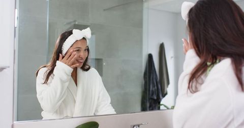 Middle-Aged Asian Woman in Bathrobe Applying Skincare by Mirror