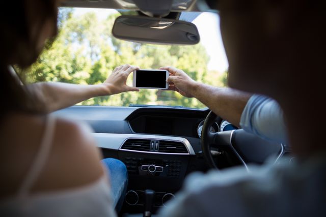 Couple taking selfie in car interior, capturing moments during a road trip. Ideal for travel blogs, social media posts, and advertisements promoting road trips, car safety, and technology use while traveling.