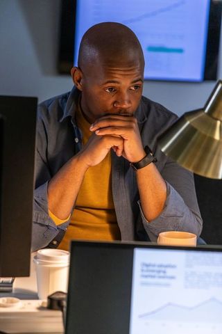 Focused african american professional analyzing financial charts on multiple monitors