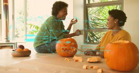 Black women carving pumpkins together in sunlit cozy kitchen