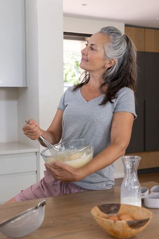 Senior woman whisking batter at sunlit kitchen counter, relaxed home baking moment