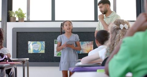 Confident Schoolgirl Presenting to Classmates with Teacher - Download Free Stock Images Pikwizard.com