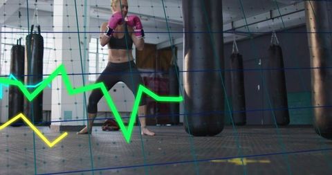 Training female boxer wearing pink gloves and leggings with data overlay and punching bags