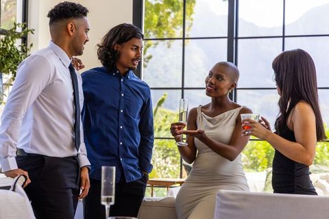 Professionals networking over champagne and cocktails in sunlit modern living room lounge