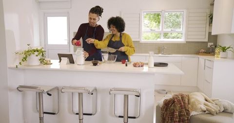 Couple baking in bright modern kitchen following tablet recipe, pouring ingredients