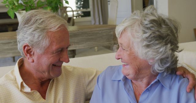 Caucasian senior couple smiling while looking at each other sitting on the couch at home - Download Free Stock Photos Pikwizard.com