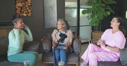 Three women recording wellness podcast in lounge with microphone and green drinks talking health