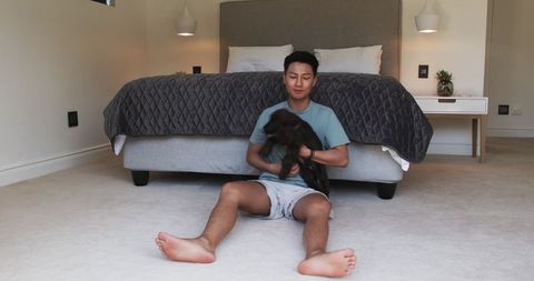 Man in minimalist bedroom holding puppy, home comfort scene